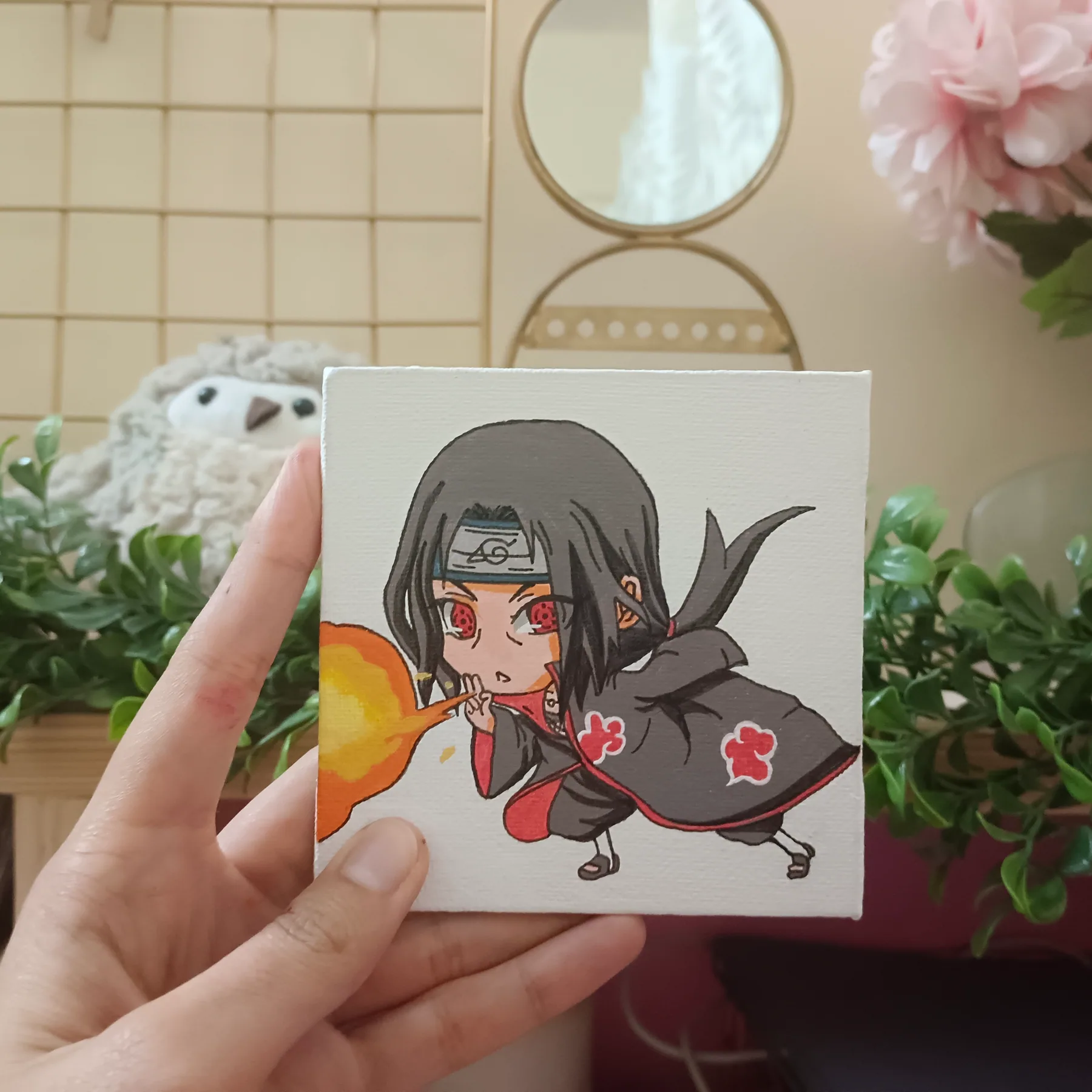 Handheld acrylic chibi mini canvas of Itachi Uchiha from Naruto on a warm yellow background near plants.