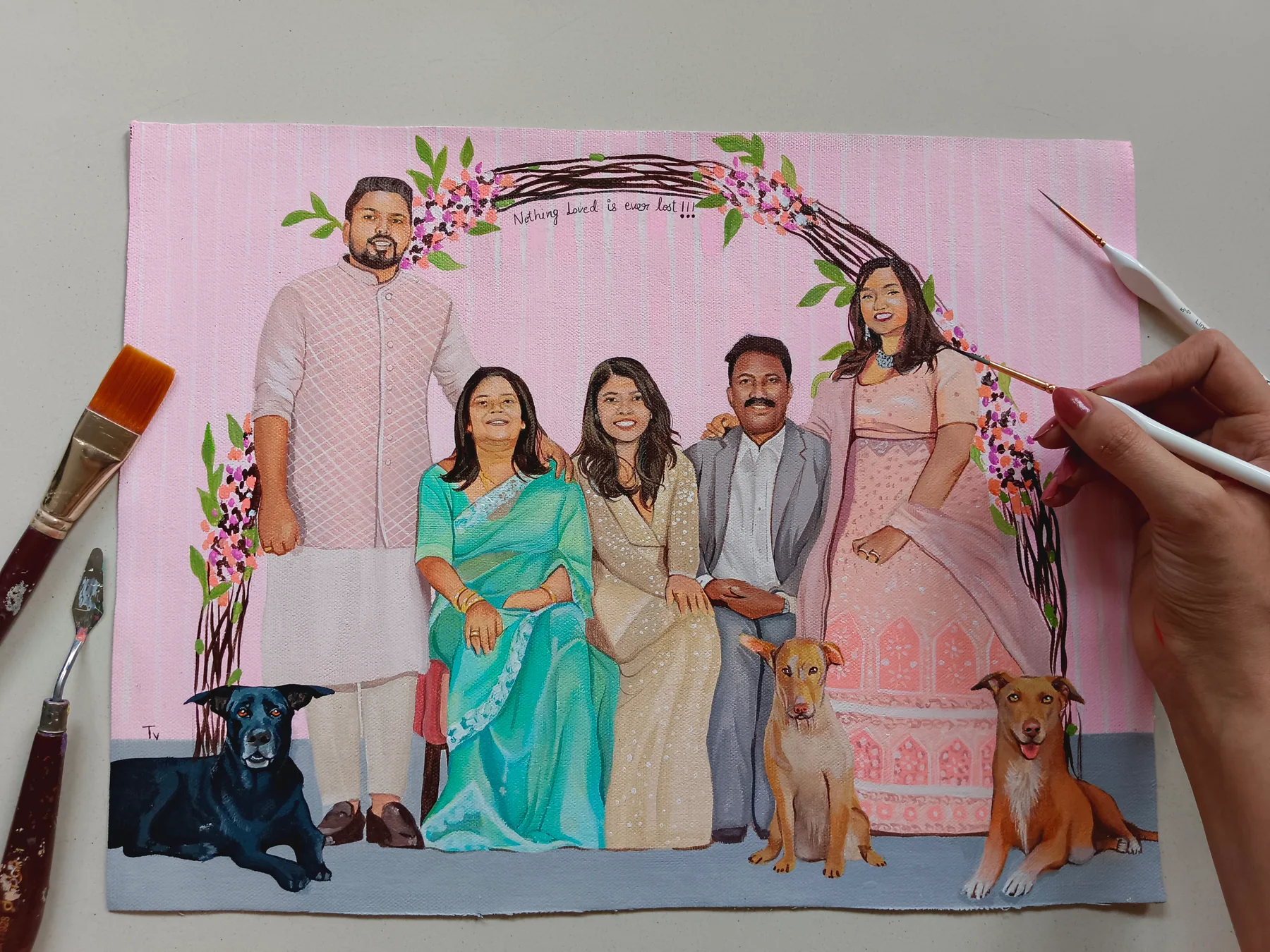 Custom family portrait painting with pets, floral decor and soft outfits, shown in progress with a brush nearby.