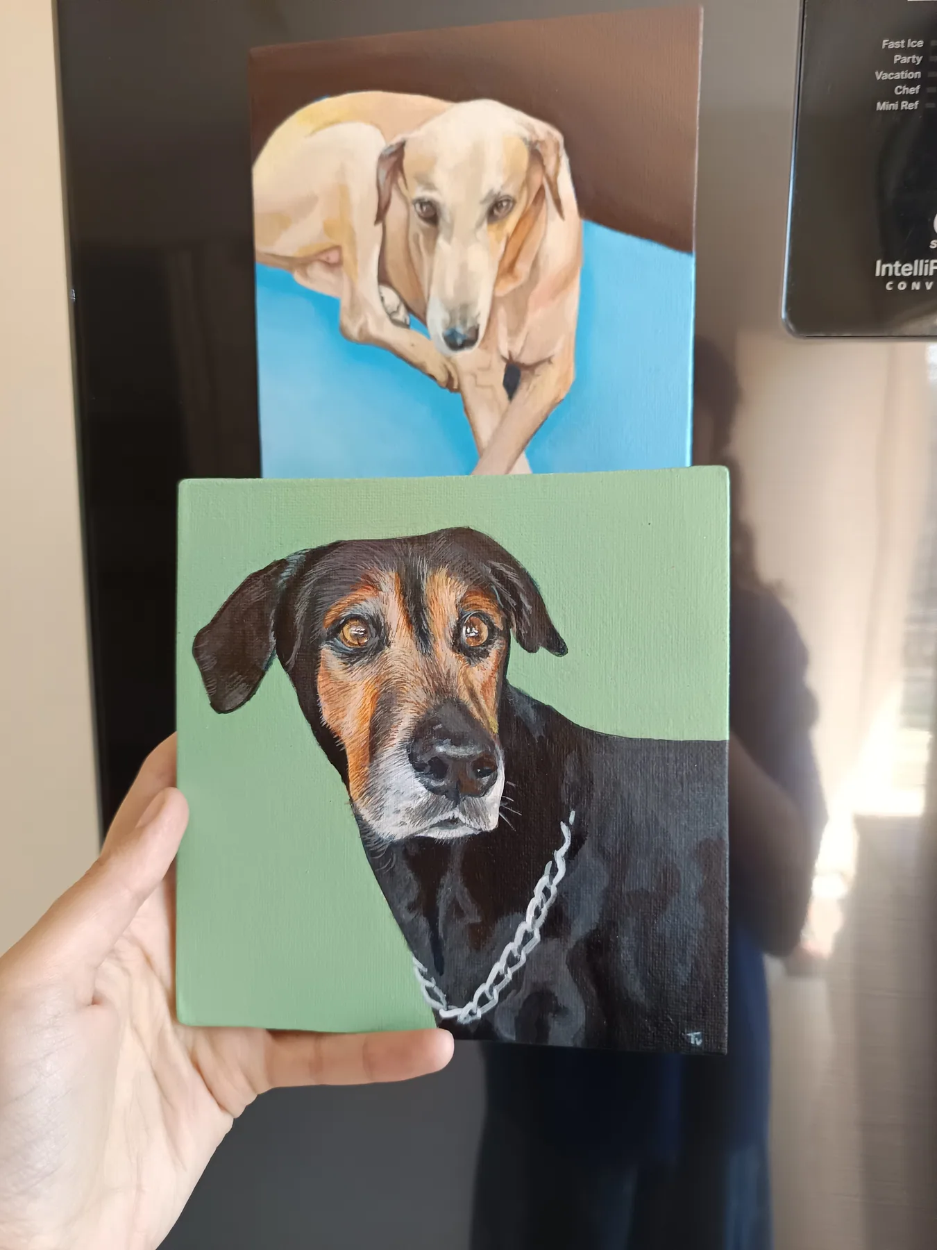 Two custom dog portrait mini canvases, one held in hand and one behind it, painted as personal pet keepsakes.