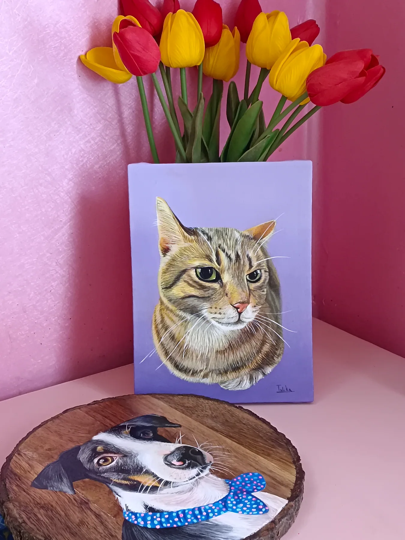 Custom pet portrait display with a cat canvas and a dog wood slice painting, styled with tulips as a warm gift sample.