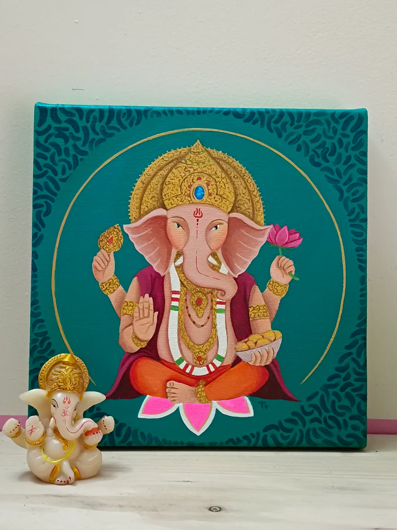 Acrylic canvas painting of Ganesha on a teal background, displayed with a small figurine for a devotional setting.