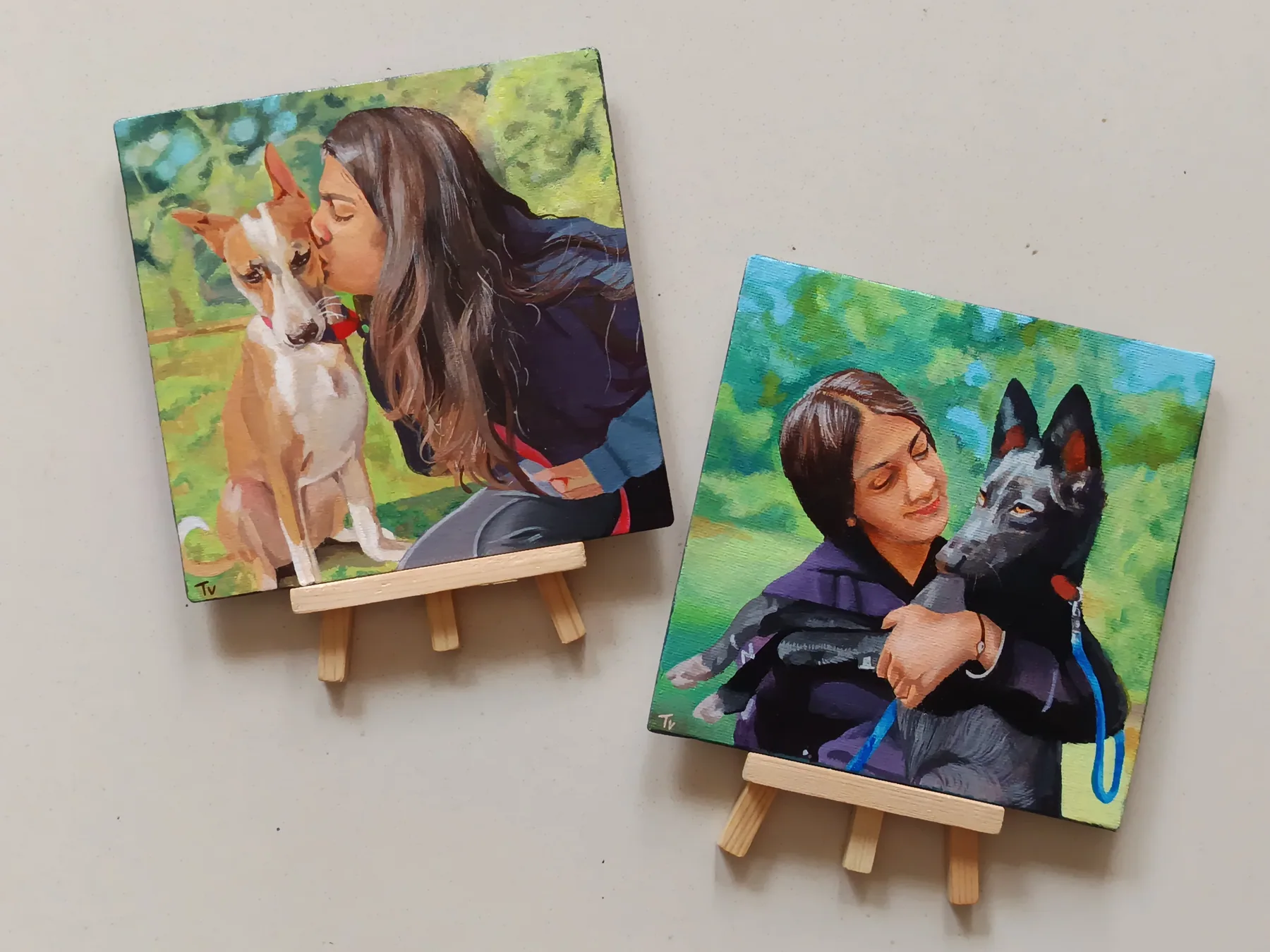 Two colourful pet portrait mini canvases showing dogs with people, displayed on easels as custom commission samples.